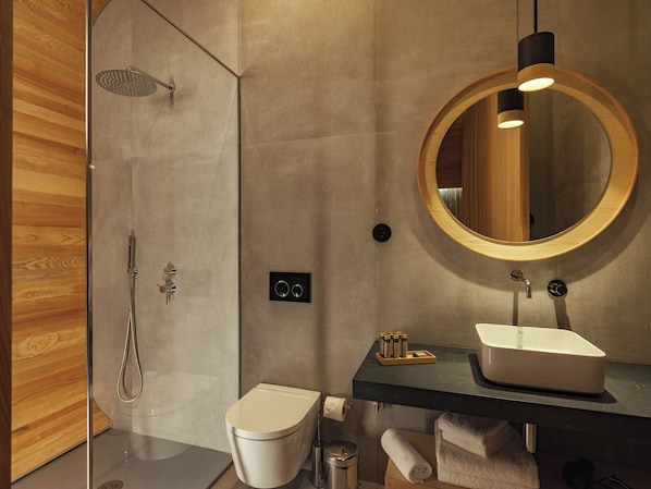 Un baño moderno con ducha de vidrio, inodoro, lavamanos con espejo y perchero para toallas.