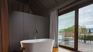 Un baño moderno con una bañera independiente, piso de madera y un amplio ventanal corredero que da a una terraza exterior.