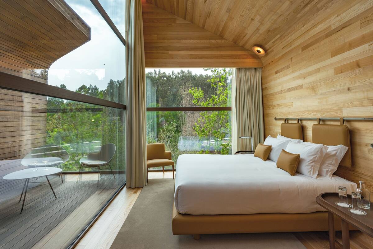 A modern bedroom with a large bed, a glass table, and a view of a forest.
