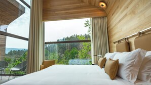 Un dormitorio con una cama grande, vistas a zonas verdes y techo de madera.