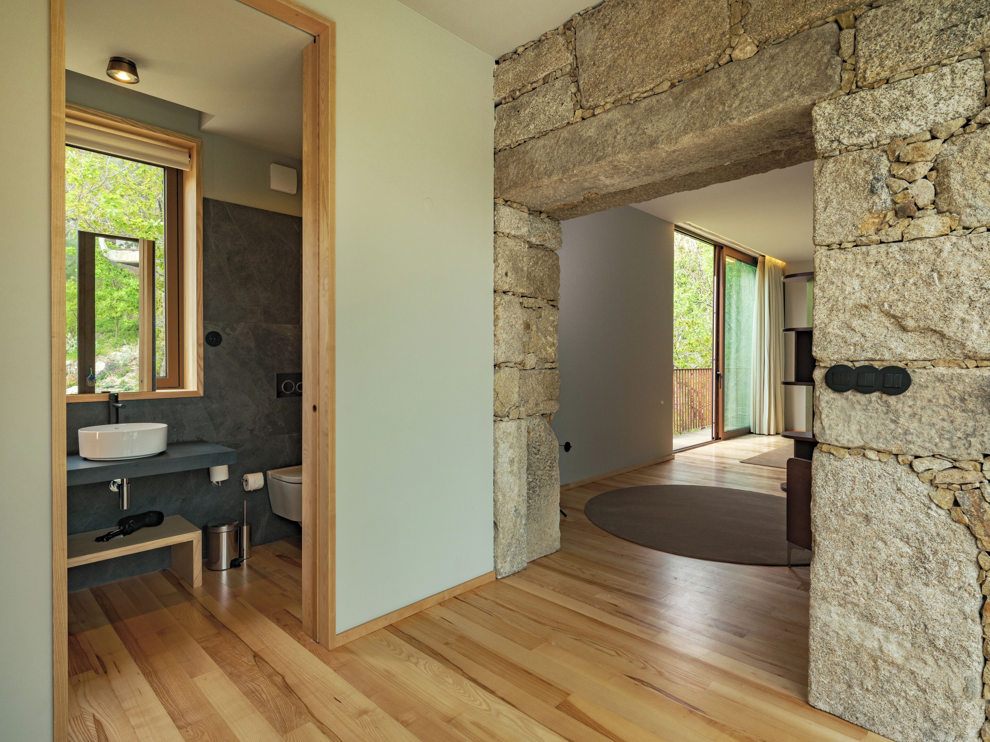 A modern bathroom with a stone archway, wooden flooring, and a large window.