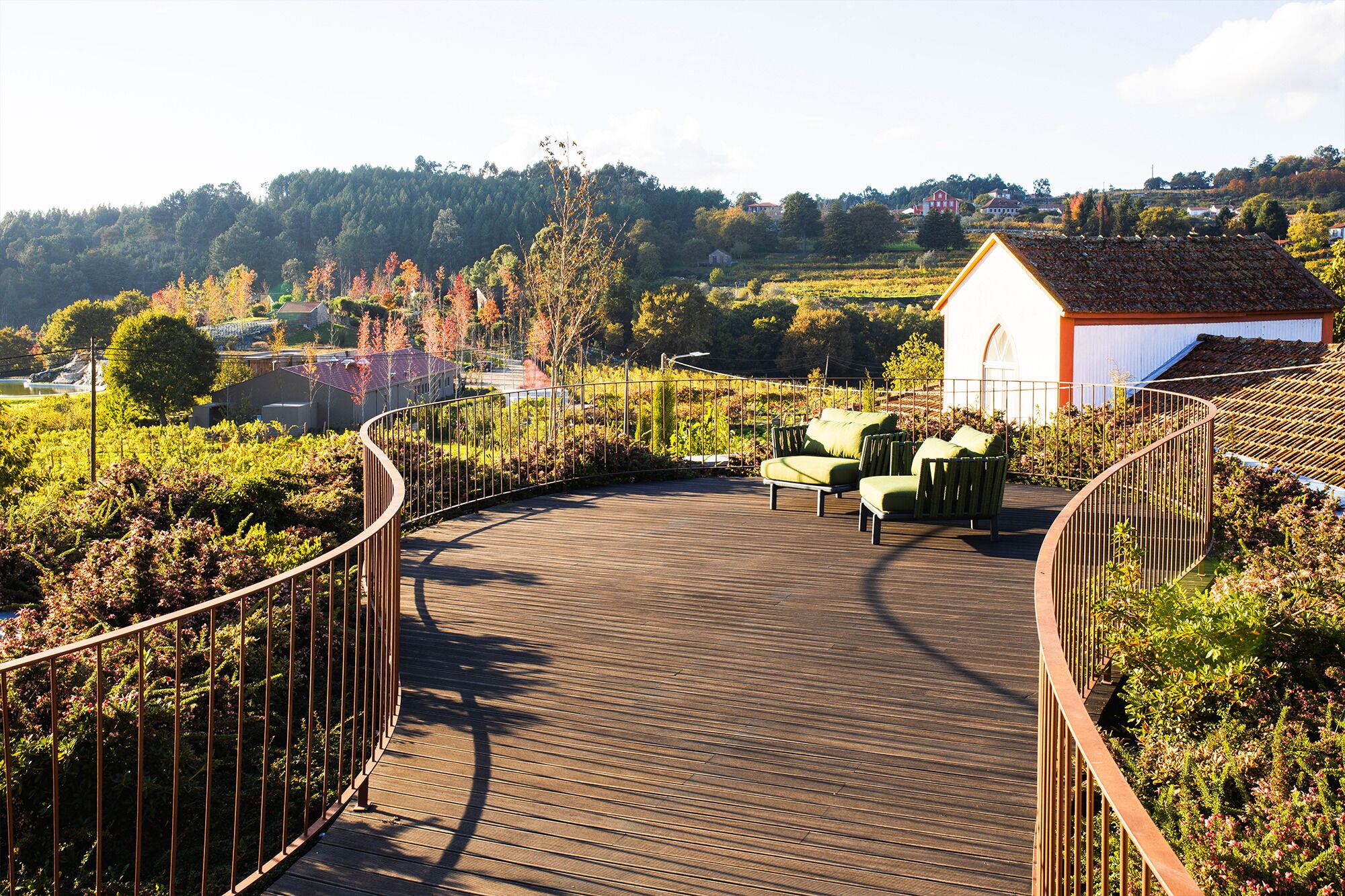 A wooden deck with a curved railing, a small white building, and green outdoor furniture.