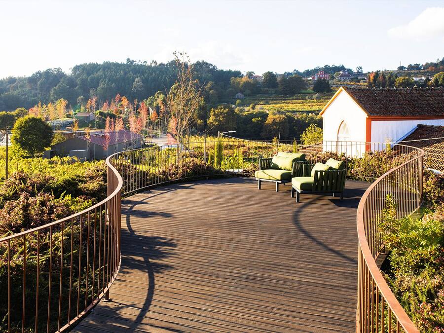 A wooden deck with a curved railing, a small white building, and green outdoor furniture.