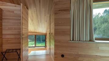 A wooden interior with a large window, a door leading outside, and a small wooden bench.