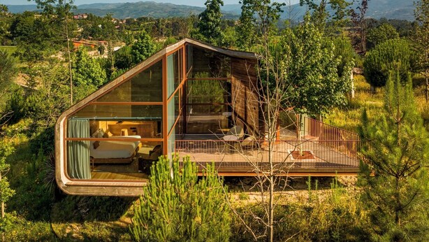 Una cabaña moderna con fachada de vidrio, una terraza y vistas del paisaje circundante.