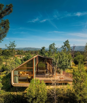 Una cabaña moderna con fachada de vidrio, una terraza y vistas del paisaje circundante.