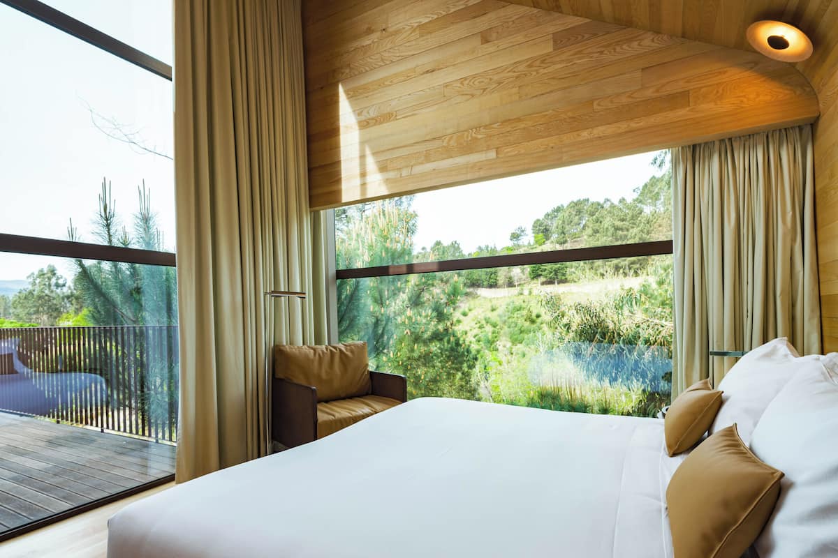 A modern bedroom with a large bed, a view of a lake, and a balcony with a wooden deck.
