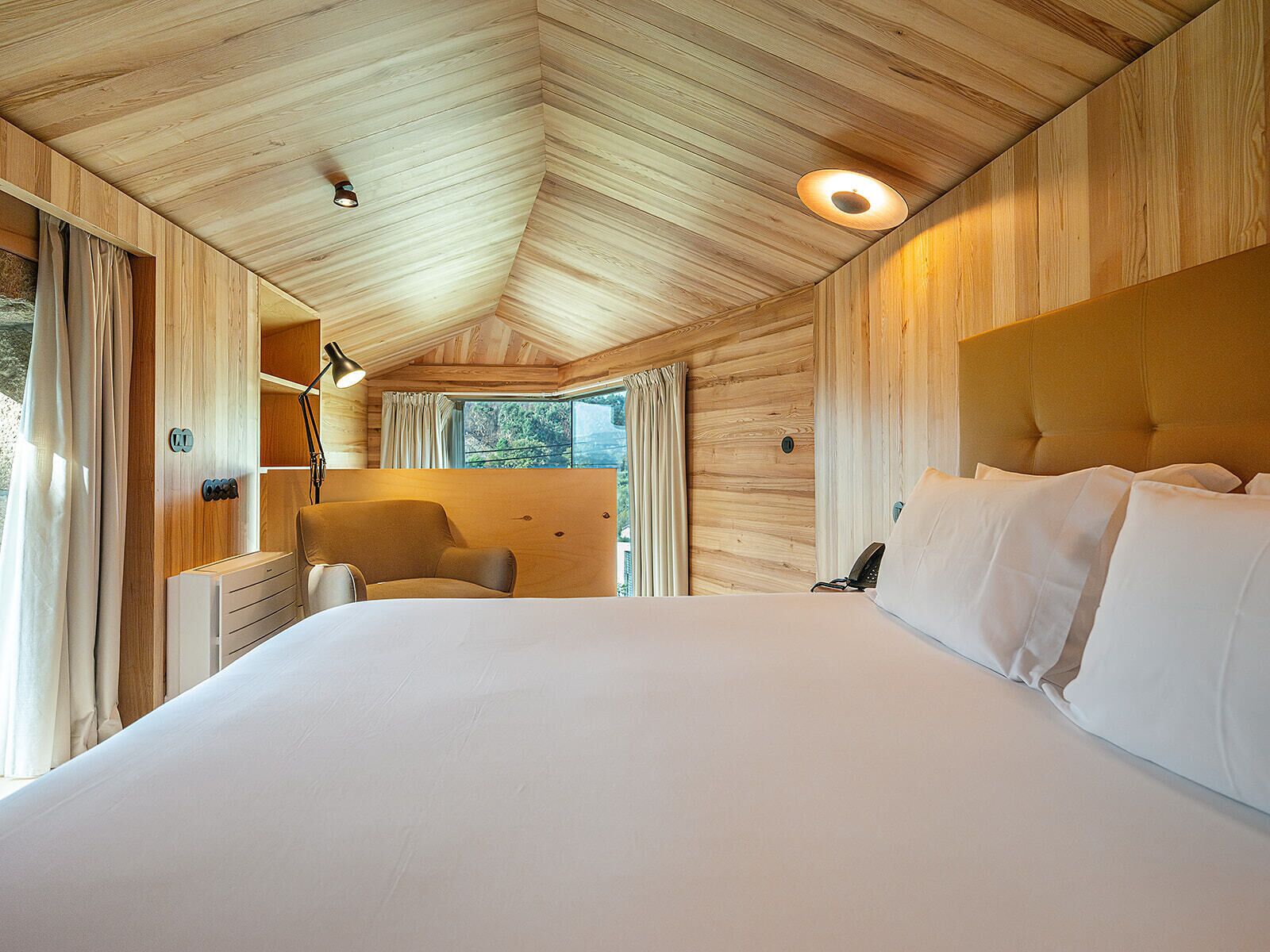 A bedroom with a large bed, a chair, a desk, and a window with curtains.