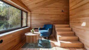 Un interior moderno con paredes de madera, un sillón azul, una pequeña mesa redonda con un florero y un piso de vidrio que conduce a una escalera.