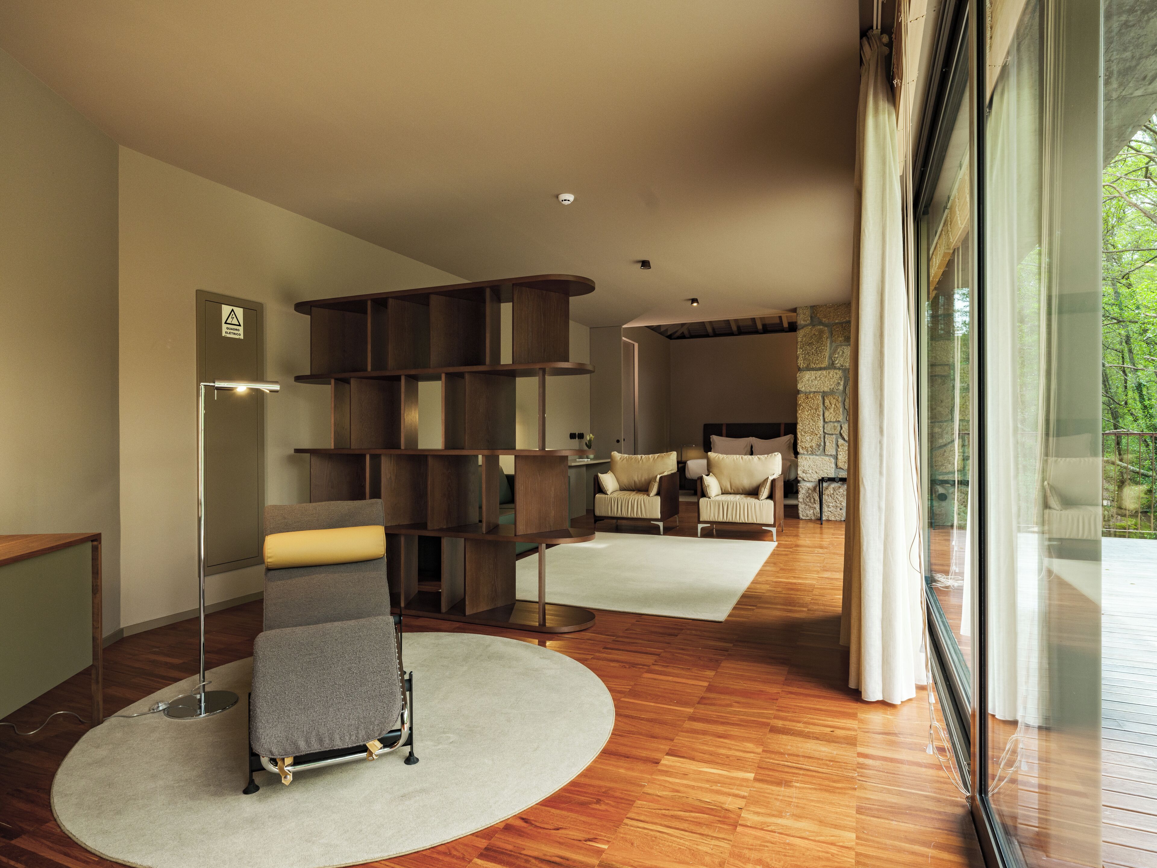 A modern living room with a wooden floor, a grey sofa, a wooden bookshelf, and a stone wall.