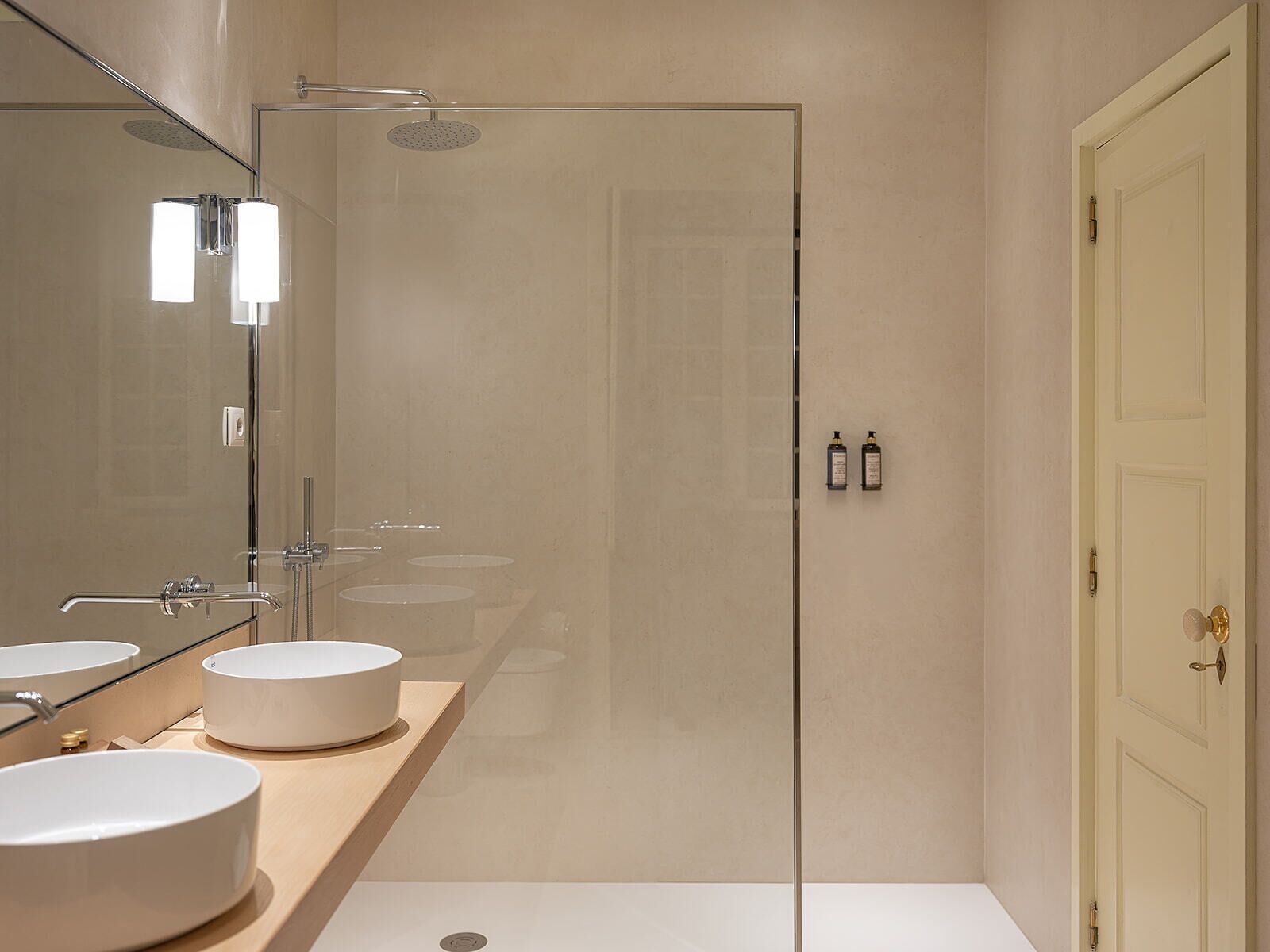 A modern bathroom with two sinks, a large mirror, a shower, and a toilet.