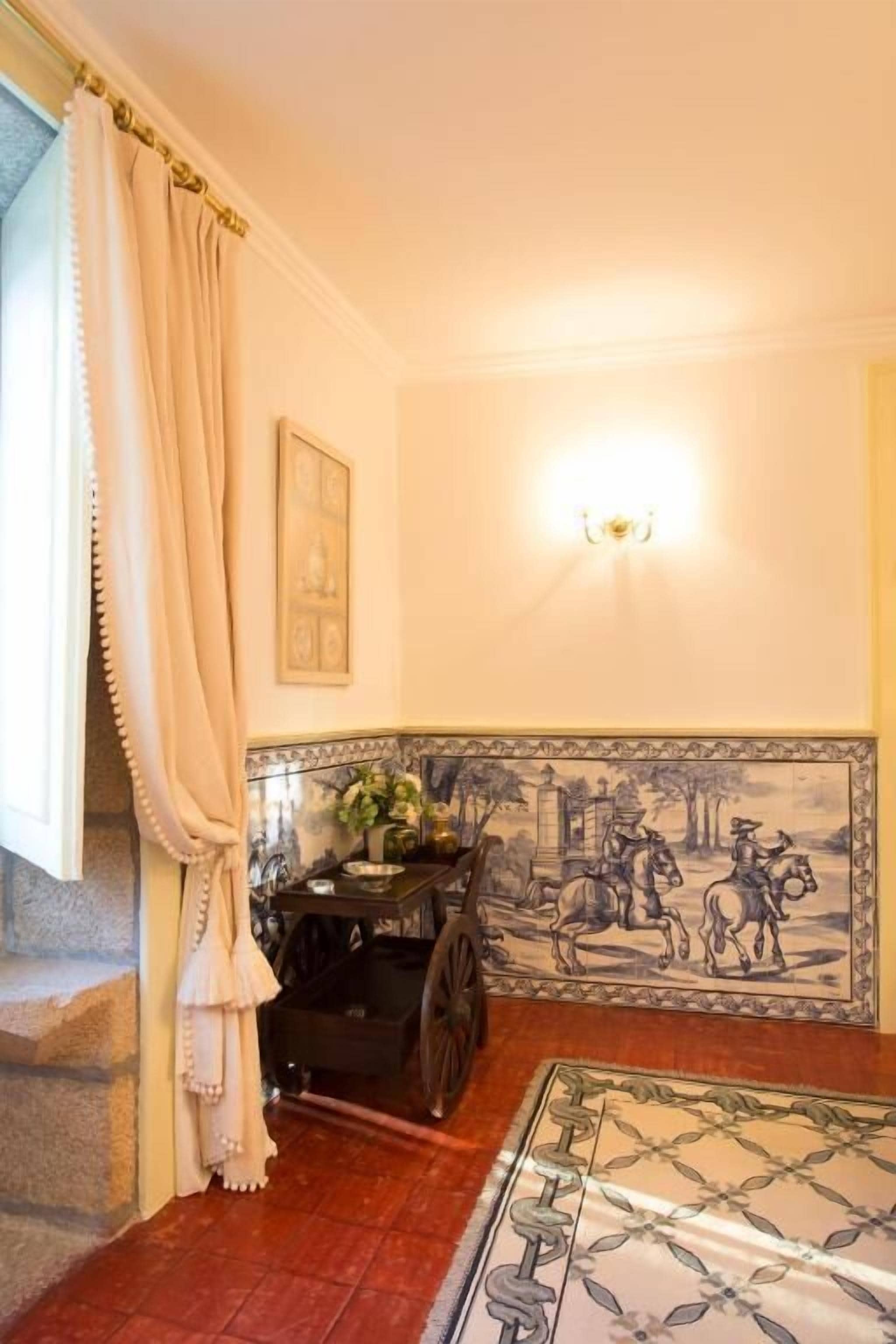 A room with a tiled wall mural, a black wooden cabinet, a patterned rug, and a window with curtains.