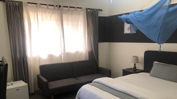 Et hotelværelse med seng, sofa, natbord, lampe og et vindue med gardiner.