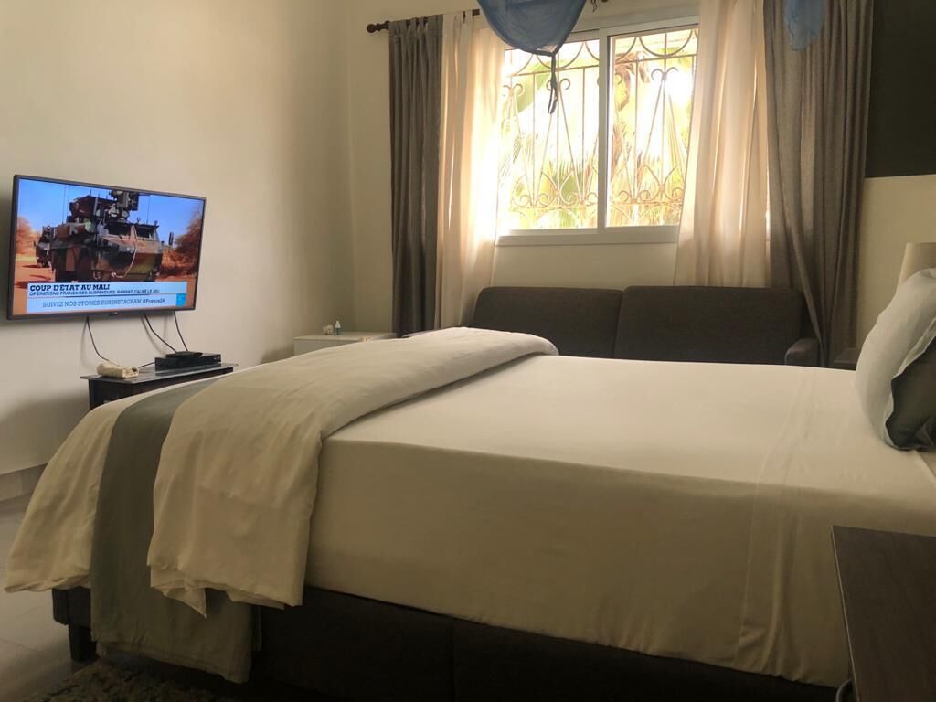 A bedroom with a bed, a TV on the wall, a window with curtains, and a bedside table.