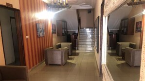 Et hotellobby med trappe, siddeområder og et stort spejl der reflekterer rummet.
