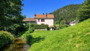 A house with a sloped roof, a small garden, and a stream. - La Maison de la Cleurie, Gîte Jusqu'à 14 Personnes (Gérardmer)