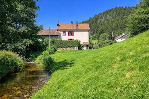 Ein Haus mit einem geneigten Dach, einem kleinen Garten und einem Bach.
