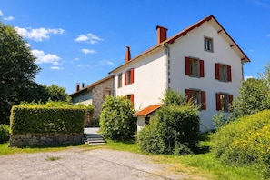 Une maison à deux étages avec une façade en pierre, des volets rouges et un toit recouvert de tuiles rouges.
