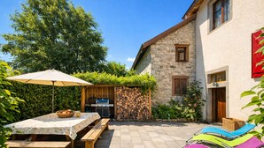 A patio with a table and benches, a barbecue grill, and colorful chairs. - La Maison de la Cleurie, Gîte Jusqu'à 14 Personnes (Gérardmer)