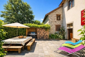 Une terrasse avec une table et des bancs, un barbecue et des chaises colorées.