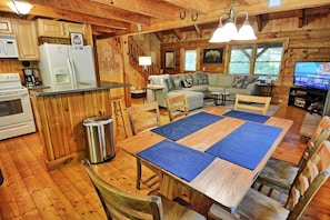 A cabin interior with a wooden dining table, kitchen area, and a sofa.