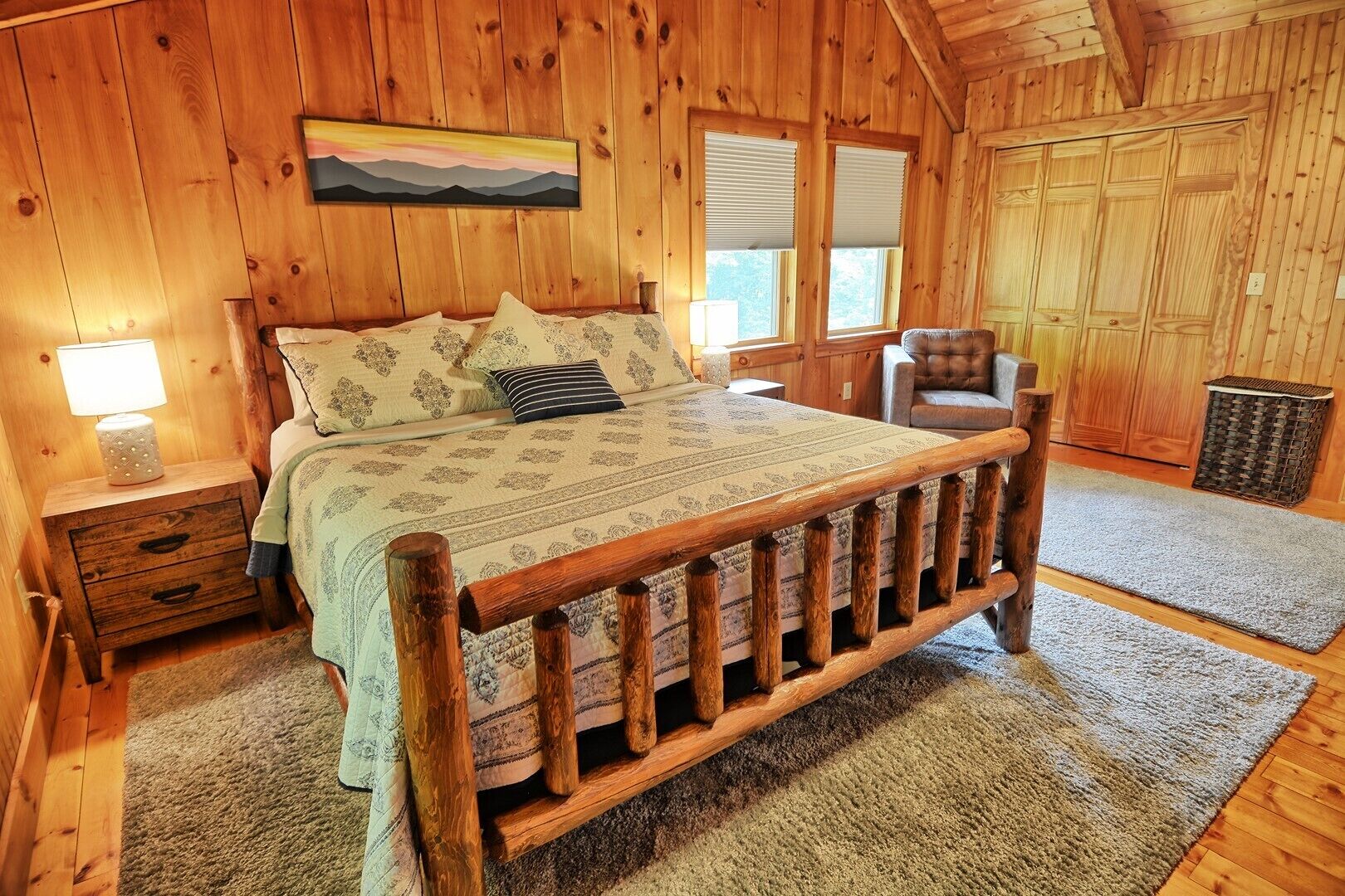 A wooden cabin bedroom with a bed, nightstands, a chair, and a window.