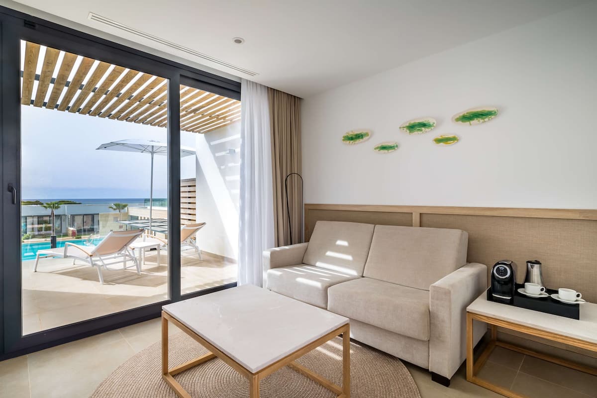 Habitación de hotel moderna con sofá, una mesita y vistas a una piscina y al océano.