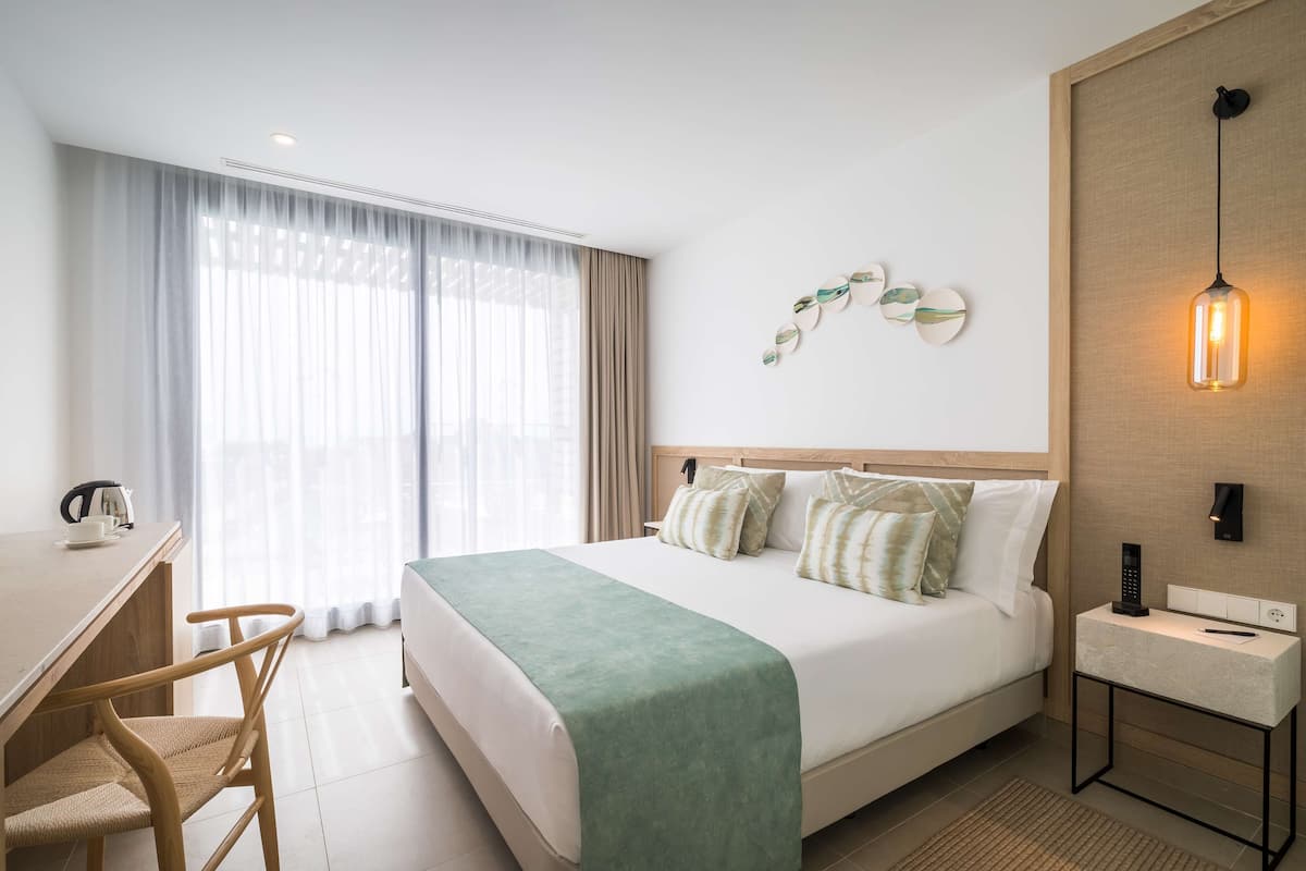Una habitación de hotel con cama, escritorio, silla, mesita de noche y lámpara de pared.