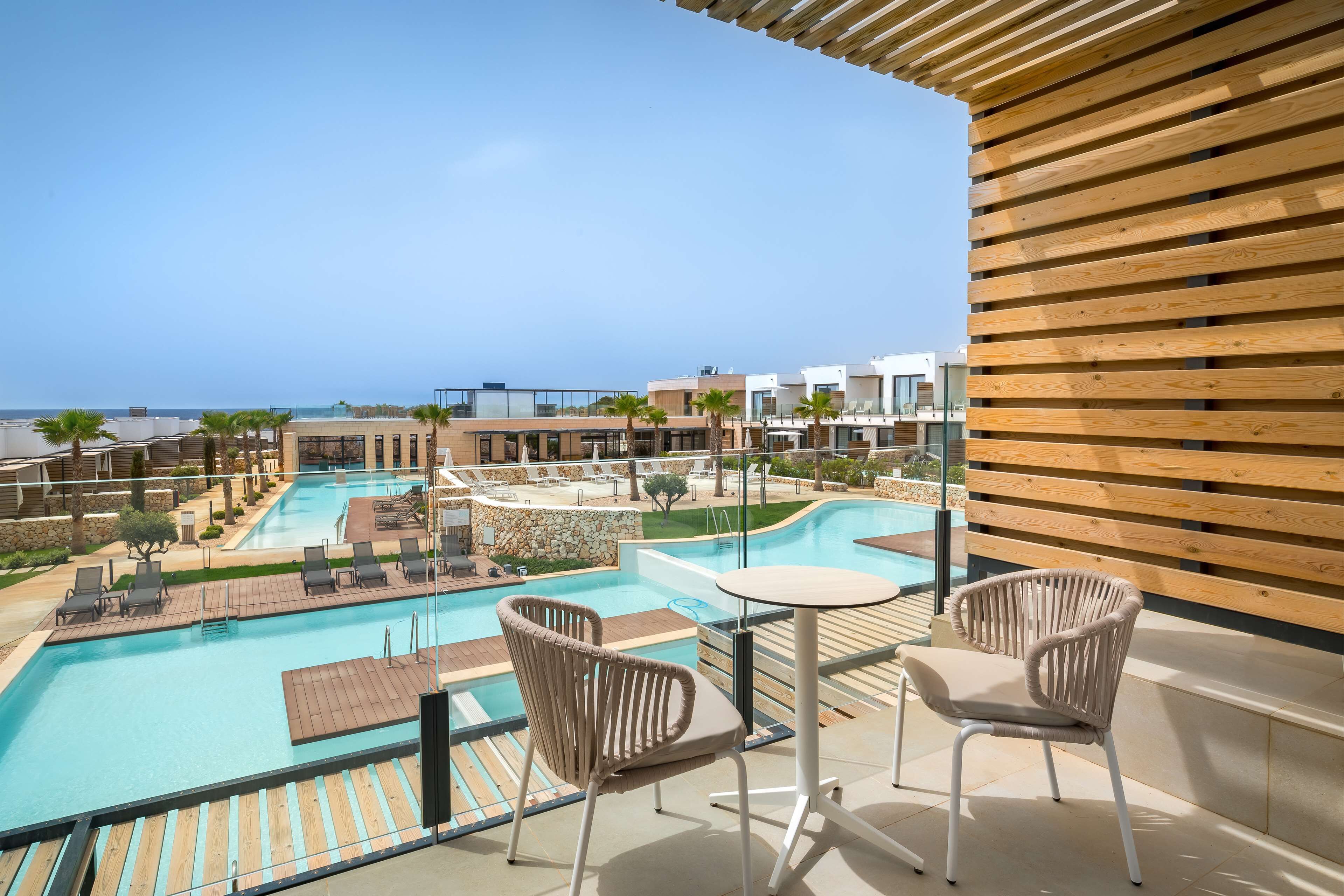 Zona de piscina en la azotea con sillones reclinables y una mesa, con vistas a una gran piscina y al océano.