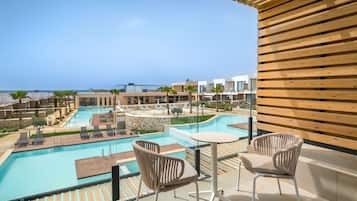 Zona de piscina en la azotea con sillones reclinables y una mesa, con vistas a una gran piscina y al océano.