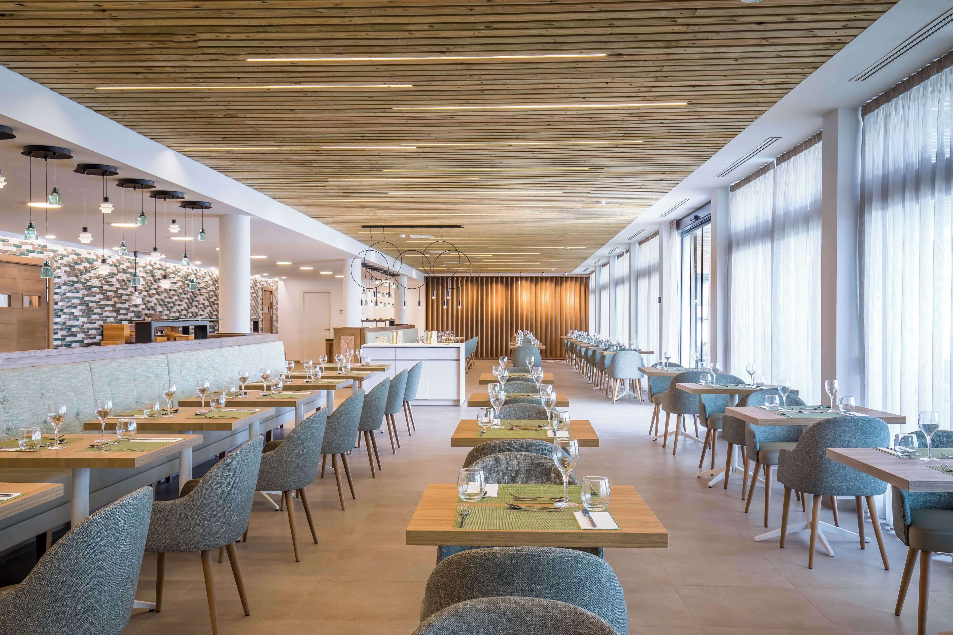 A modern restaurant with long tables, chairs, and a bar area.
