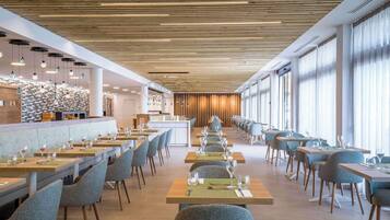 A modern restaurant with long tables, chairs, and a bar area.