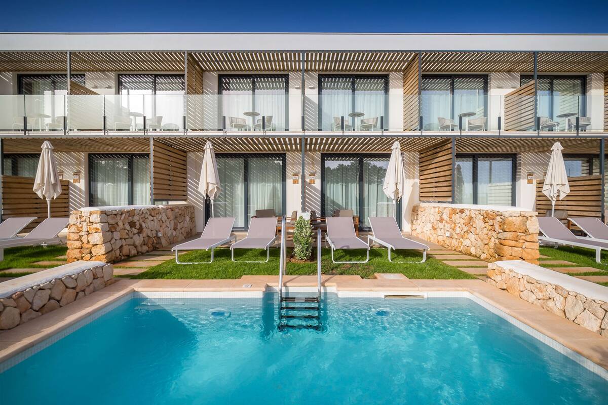 Un hotel moderno con piscina, sillas de descanso y un muro de piedra.