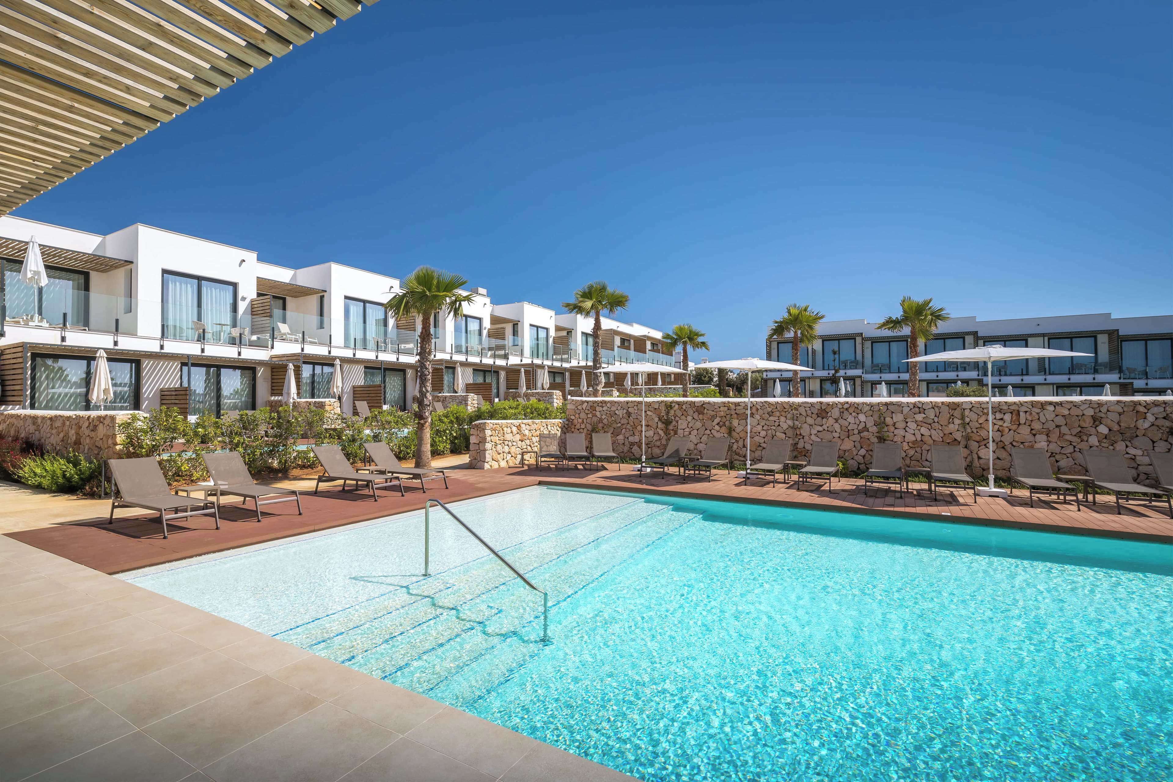 Un hotel moderno con piscina, sillones de descanso y palmeras.