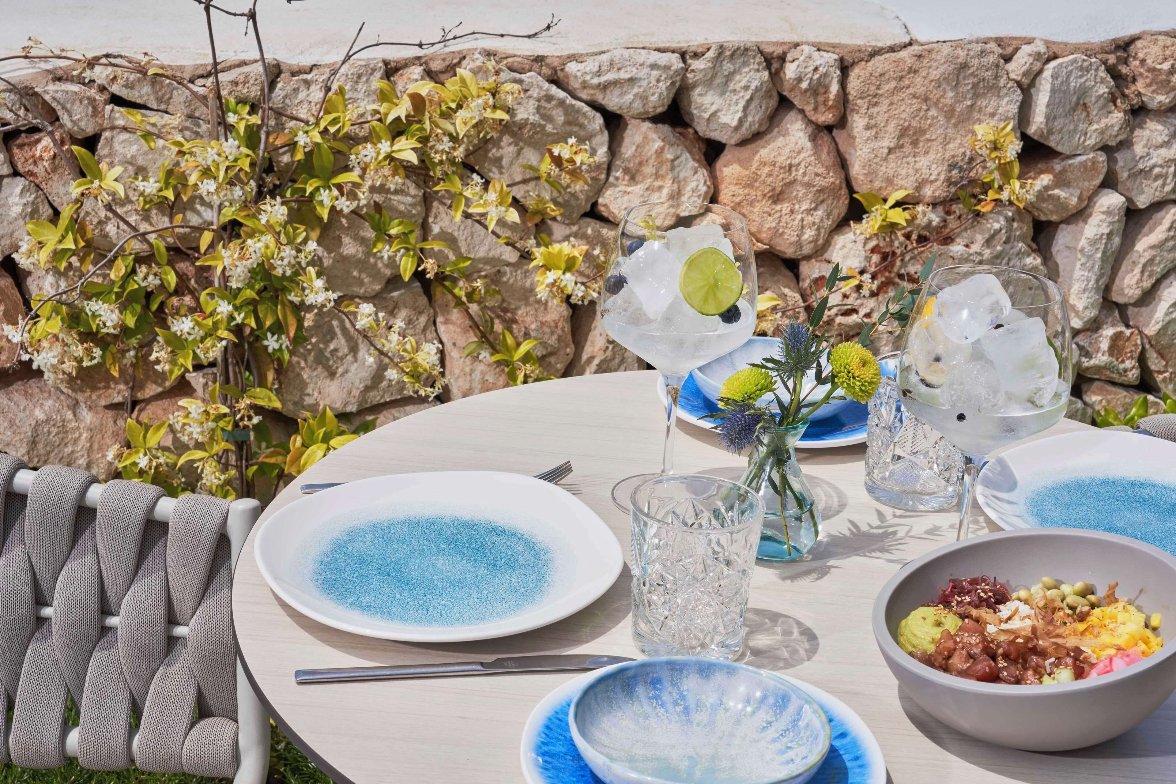 Una mesa al aire libre con platos, un tazón y vasos de agua con hielo.
