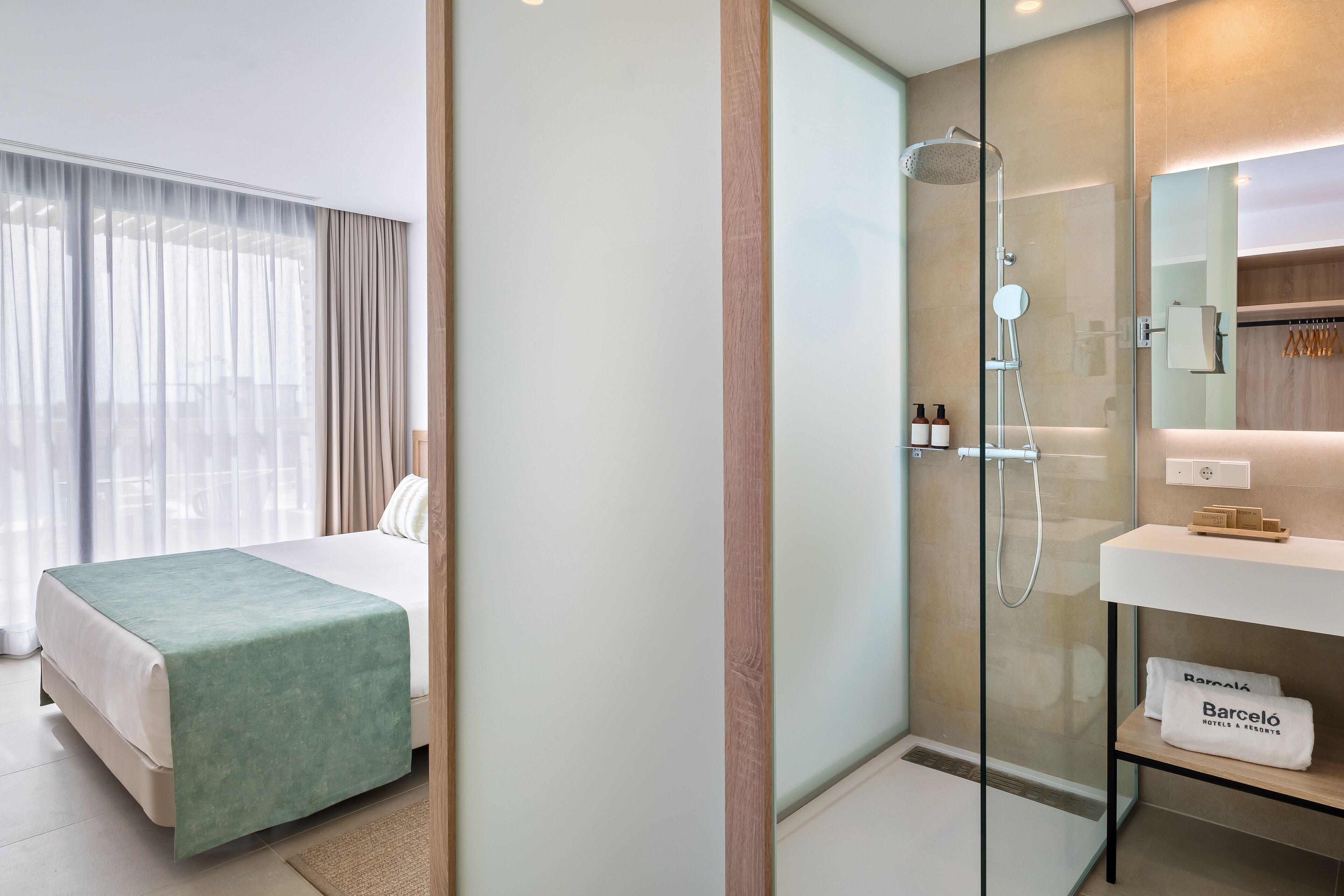 A hotel room with a bed, a shower area, a vanity with a mirror, and a sign that reads "Barcelo Hotels & Resorts".