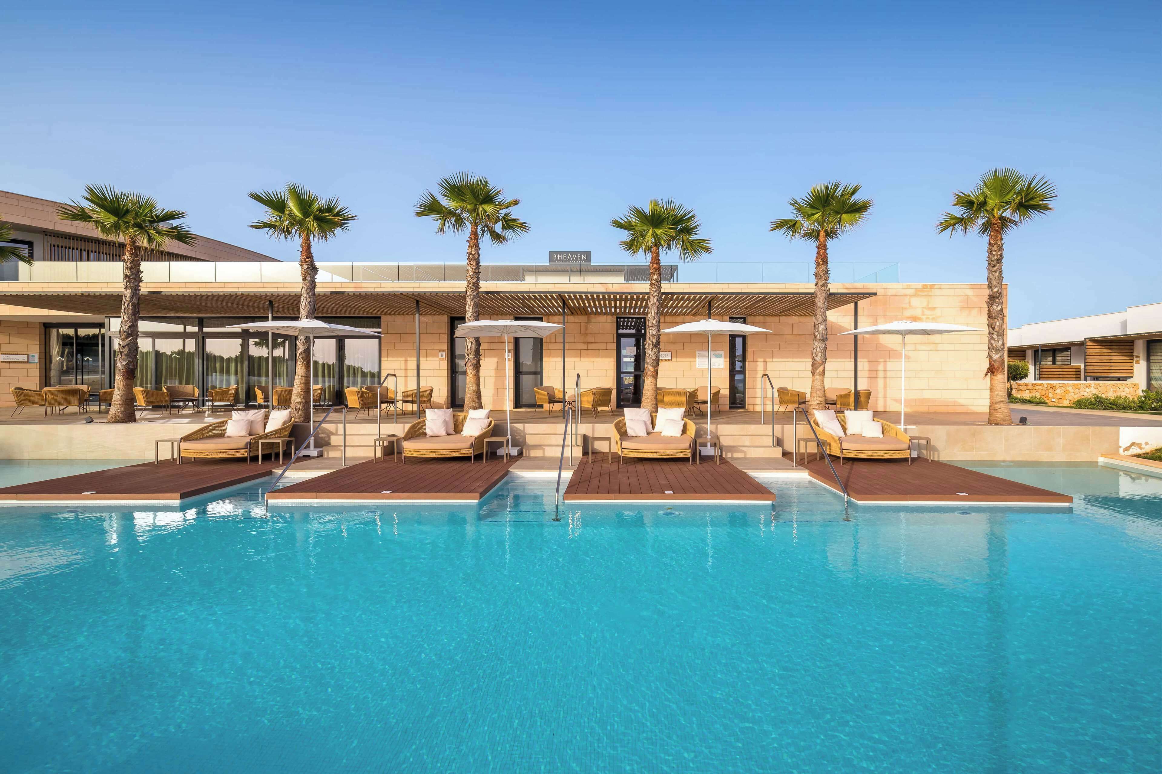 A modern hotel with a pool area, palm trees, and sun loungers.
