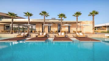 Un hotel moderno con zona de piscina, palmeras y tumbonas.