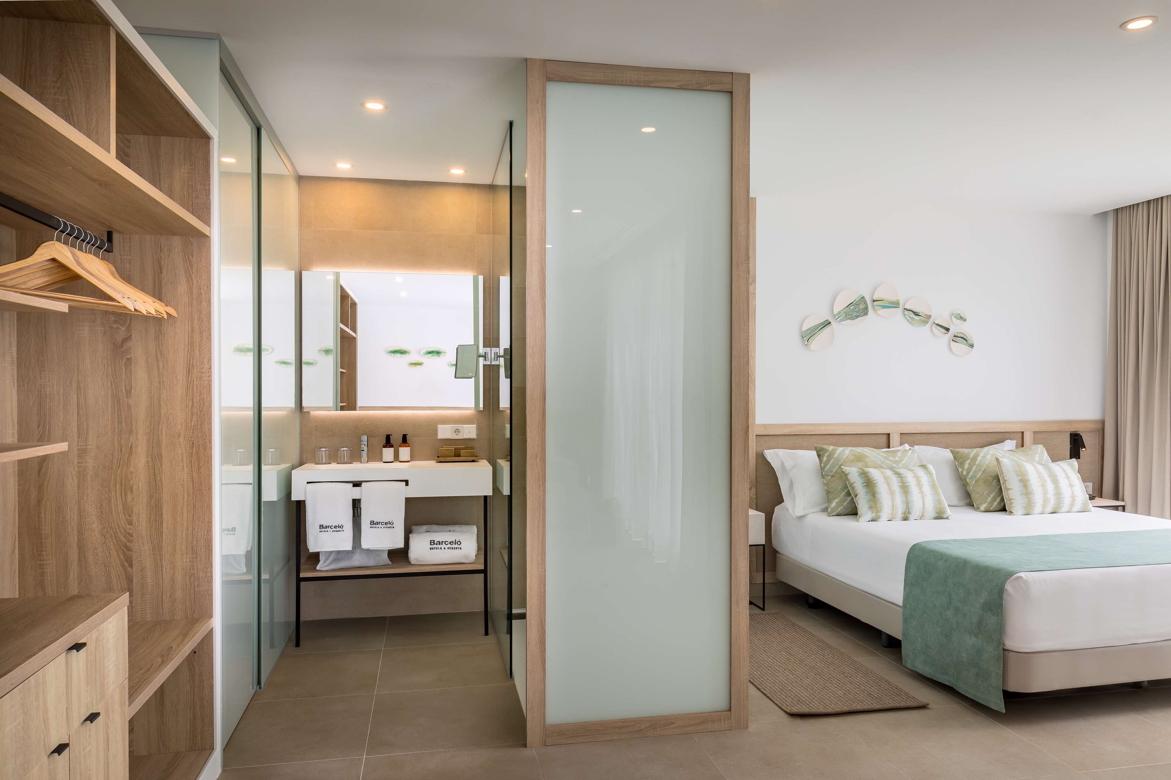 A modern hotel room with a large bed, a separate bathroom with a vanity, and a wooden wardrobe.