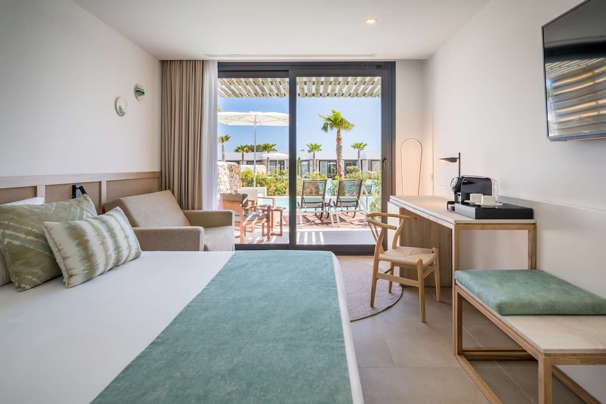Habitación de hotel con cama, escritorio, silla y vistas a una piscina y palmeras.
