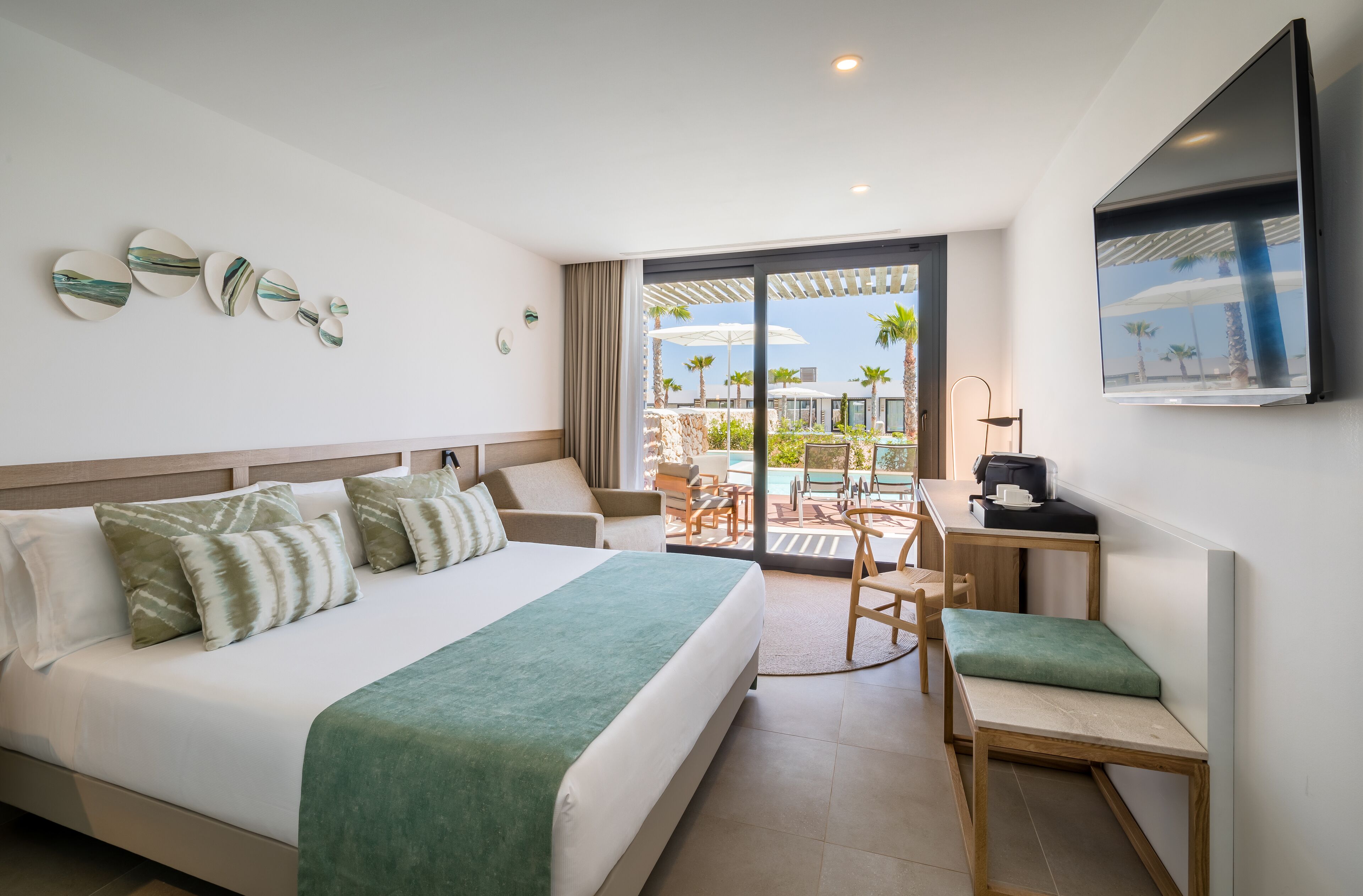 A hotel room with a large bed, a desk, a chair, and a view of the outdoor pool area.