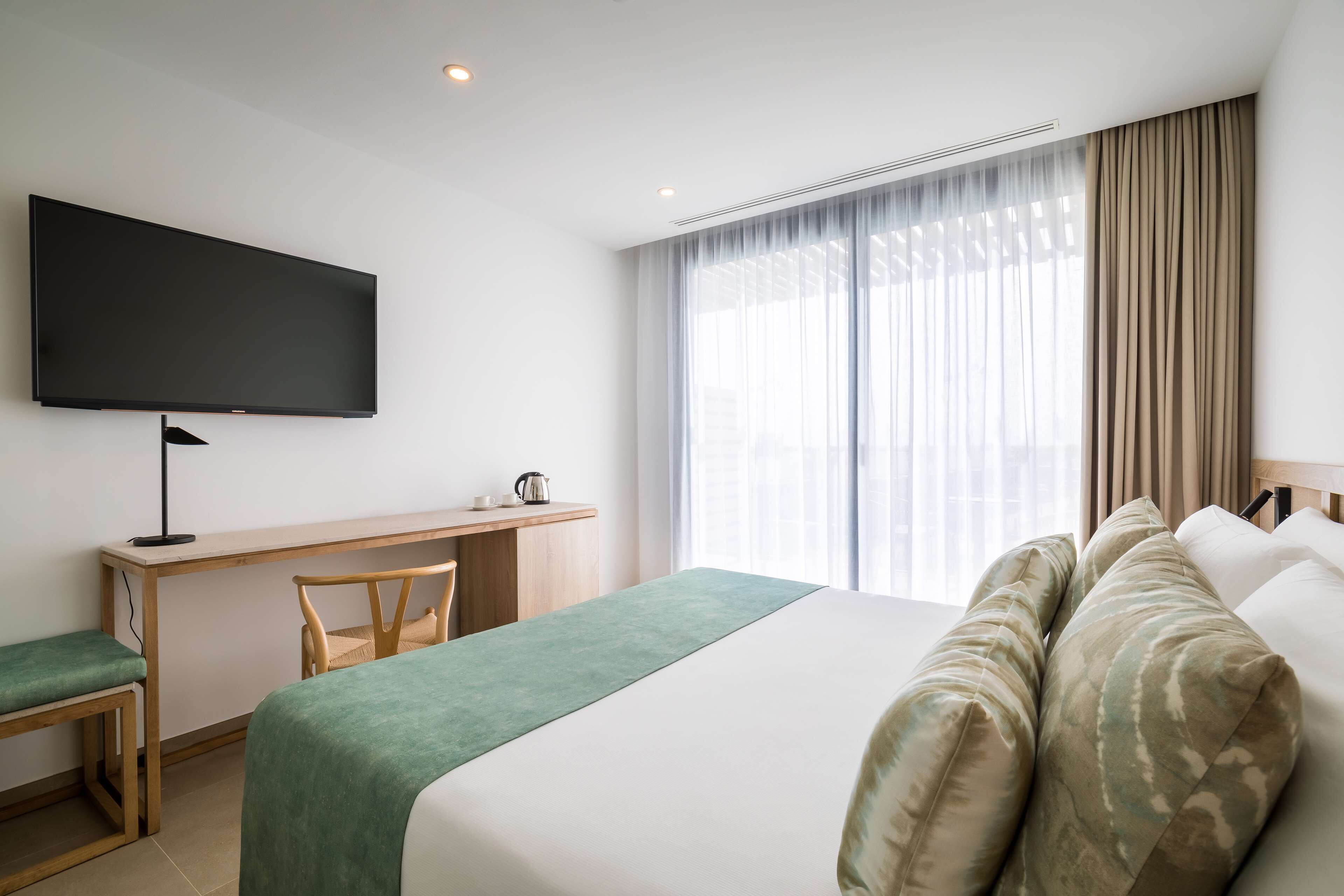 A hotel room with a bed, a desk, a chair, a television, and a window with curtains.