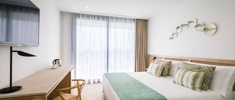 A hotel room with a bed, a desk, a chair, a TV, and a window with curtains.
