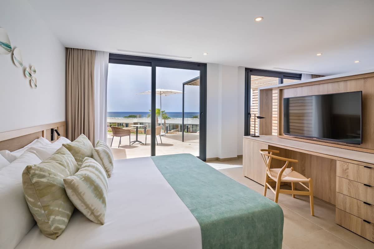Habitación de hotel con cama, escritorio, televisor y balcón con vista a la playa.