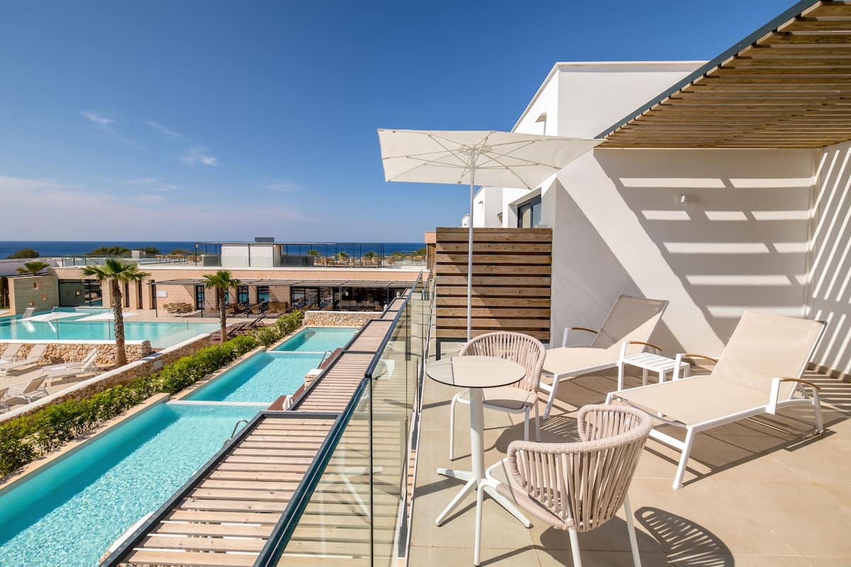 Zona de piscina en la azotea con sillones de descanso y una sombrilla, con vistas a una piscina y una playa.
