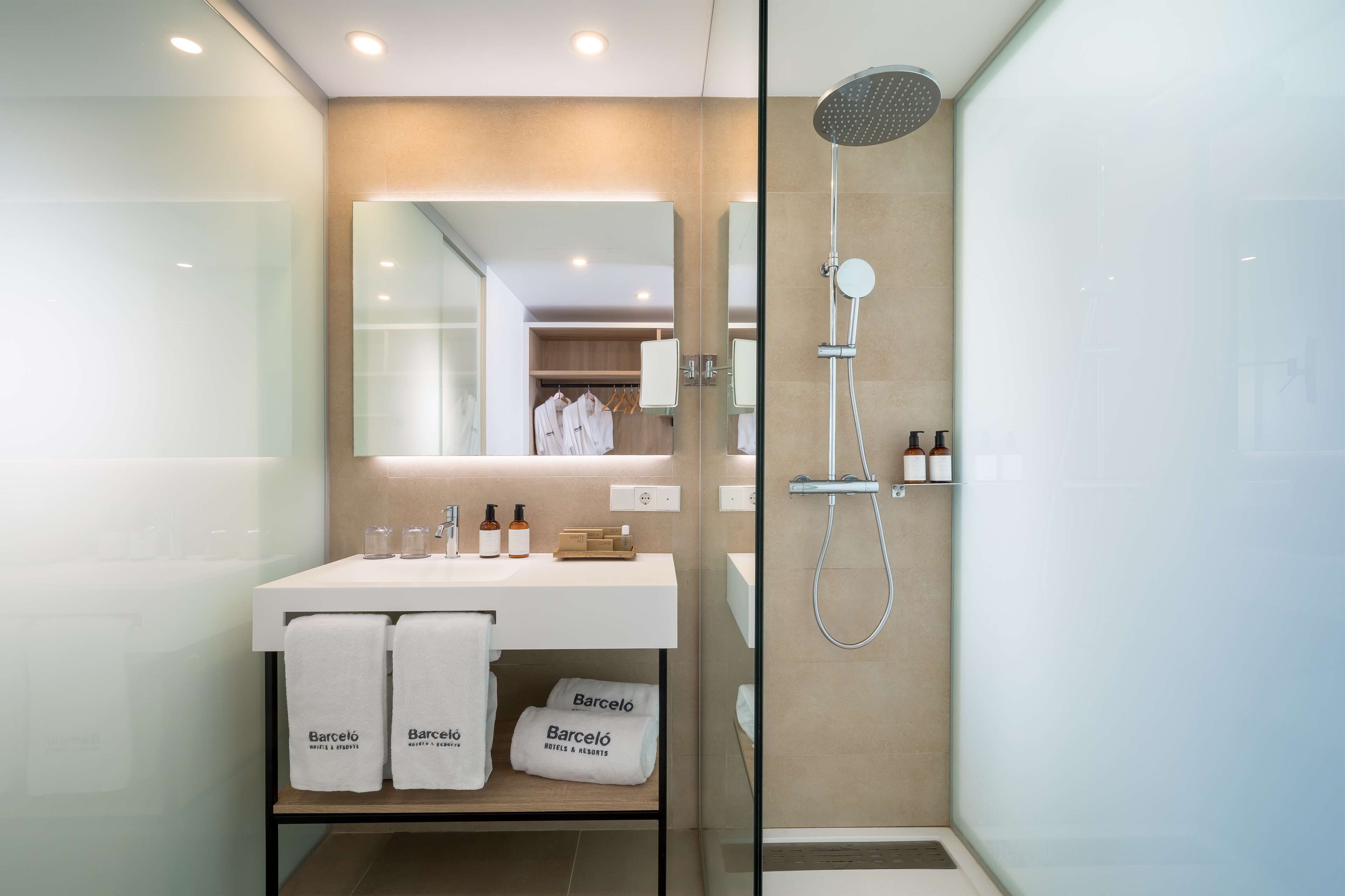 Un baño moderno con ducha envuelta en vidrio, un lavamanos blanco con artículos de aseo y un espejo sobre él.