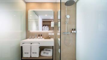 Un baño moderno con ducha envuelta en vidrio, un lavamanos blanco con artículos de aseo y un espejo sobre él.