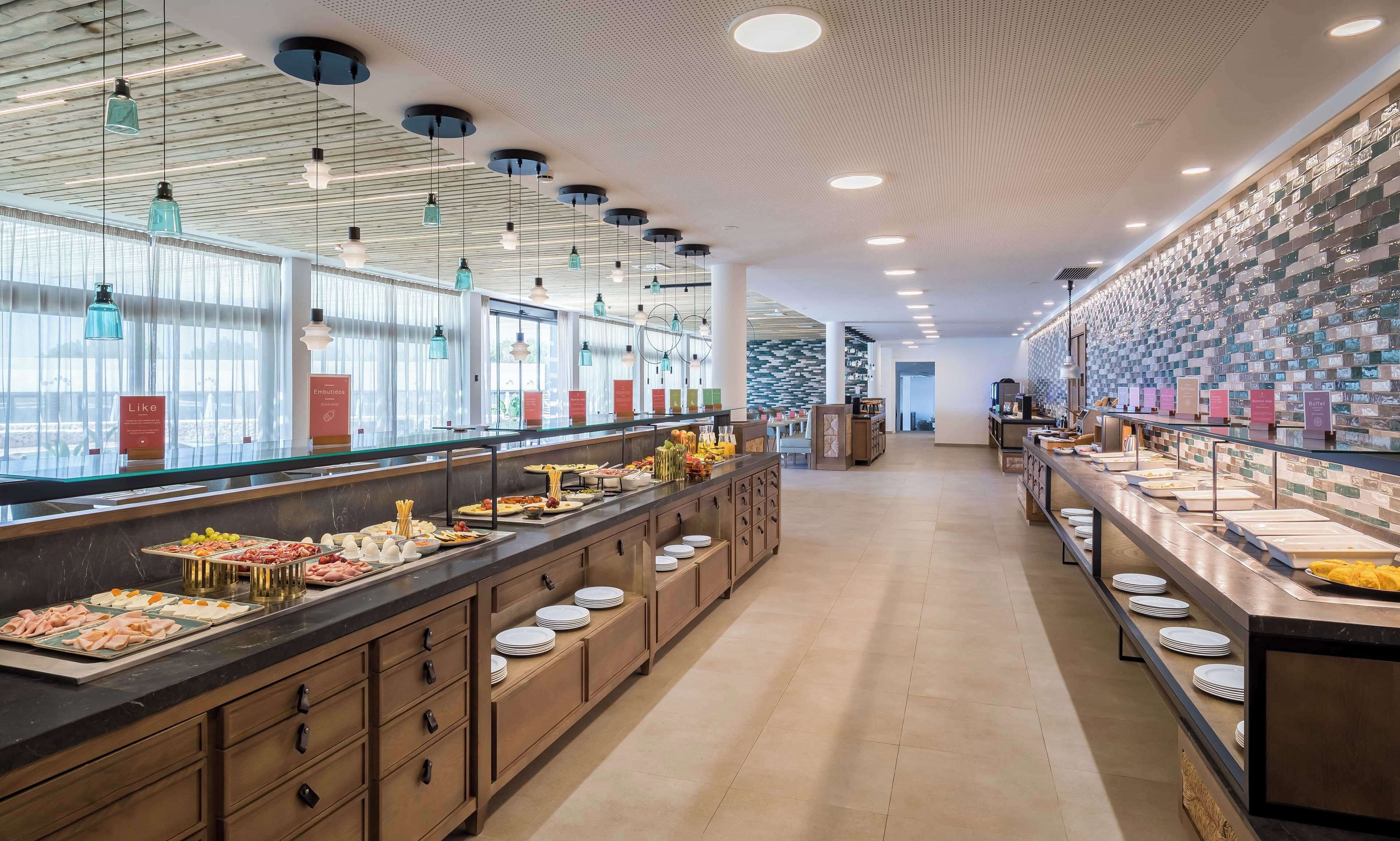 A buffet area with various food options, a counter with plates, and a wall with a patterned design.