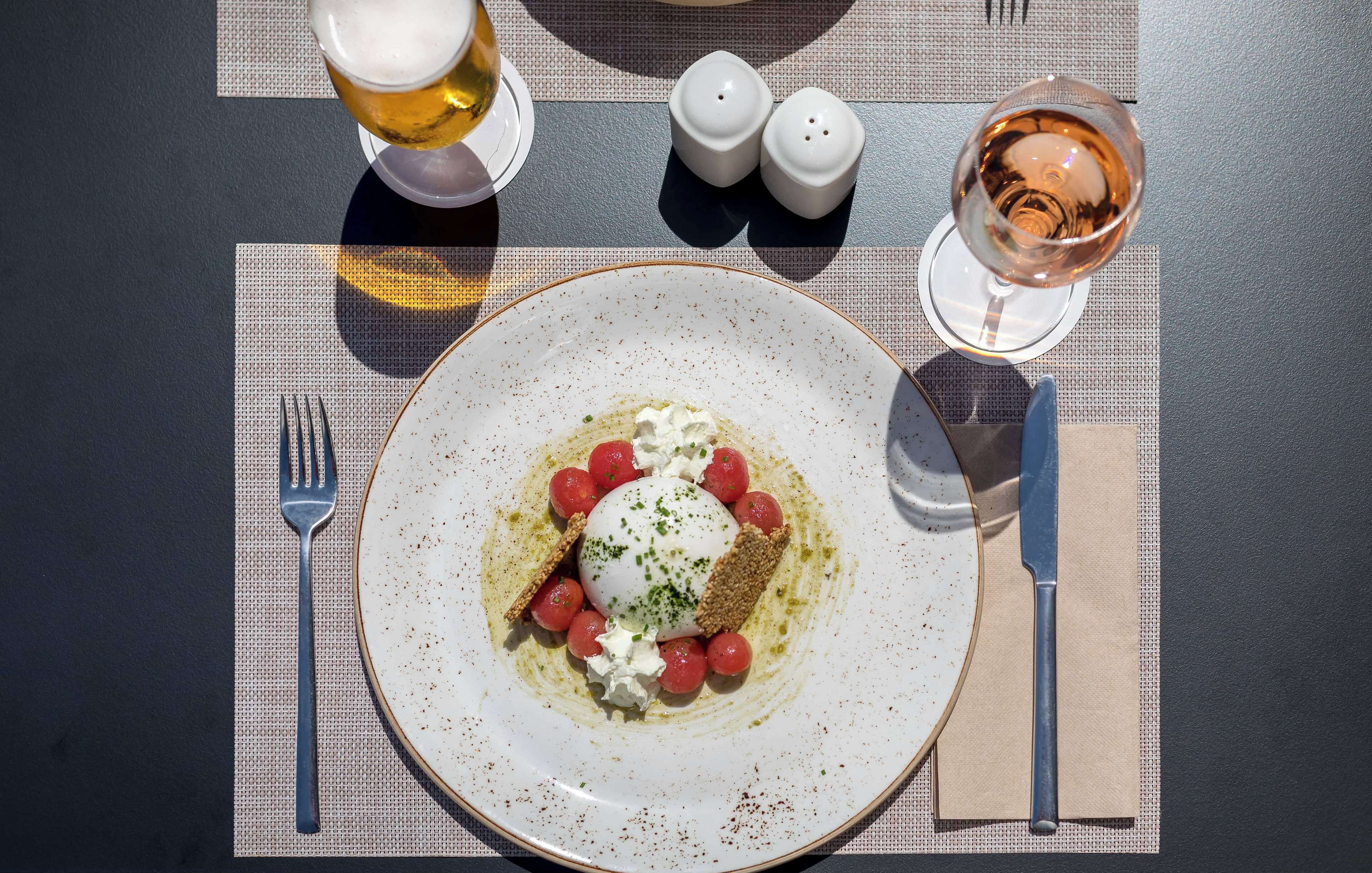 A dining table with a plate of food, a fork, a knife, two salt shakers, and a glass of wine.