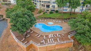 Una piscina con solárium, rodeada de árboles y un edificio al fondo.